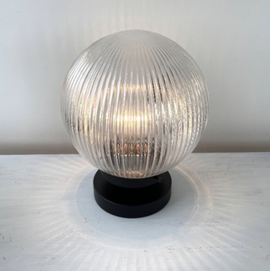 Clear ribbed glass table lamp with a black base, illuminating a white surface.