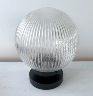 Clear ribbed glass table lamp with a black base, sitting on a white surface.