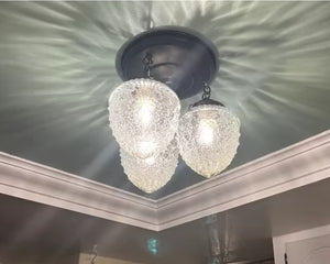 Three clear glass acorn-textured light globes illuminate a ceiling with crown molding.