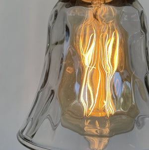 Illuminated glass pendant light fixture with a warm, glowing bulb.