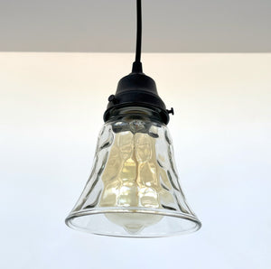 Clear glass pendant light fixture with a textured, bell-shaped shade and black metal fitting.