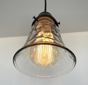Clear glass pendant light fixture with a textured design, illuminating a warm-toned Edison bulb.