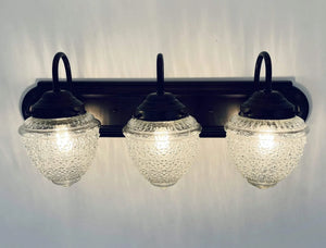 Three-light vanity fixture with antique acorn glass shades and dark bronze finish.
