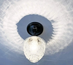 Clear glass ceiling light fixture with textured shade, black metal mount, casting shadows on a textured ceiling.