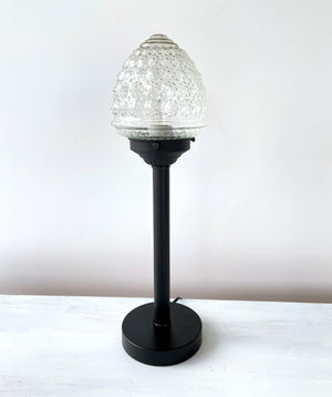Tall, antique-style table lamp with a clear, textured glass shade and a black metal base.