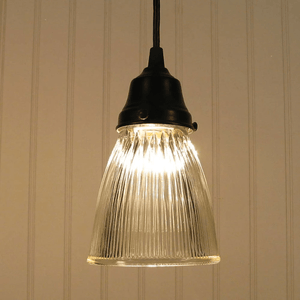 Clear ribbed glass pendant light fixture with a dark bronze finish, illuminated against a white paneled wall.