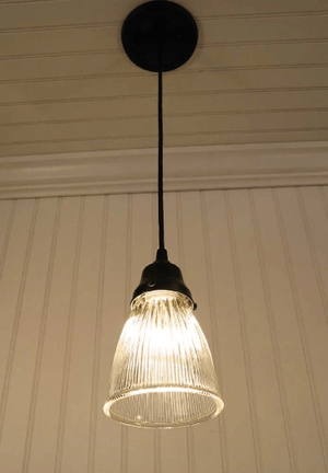 Clear glass pendant light fixture with ribbed detailing, illuminating a room with warm light against a paneled wall.