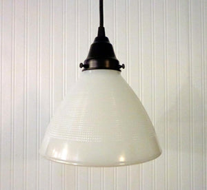Milk glass pendant light fixture with textured shade, hanging against white paneled wall.
