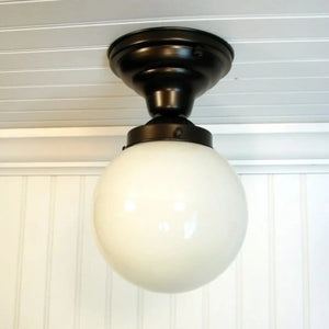 White milk glass globe ceiling light fixture with dark bronze finish, installed on white paneled ceiling.