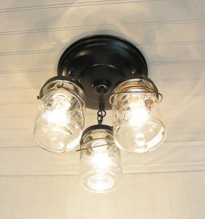 Three glass mason jar light fixture hanging from a black ceiling mount.