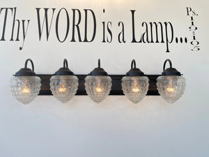 Five-light vanity fixture with clear glass shades, mounted on a dark brown base against a white wall.