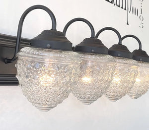 Four-light vanity fixture with clear textured glass shades and dark bronze finish.