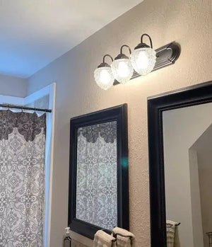 Three-light vanity fixture with clear glass acorn shades, installed in a bathroom.