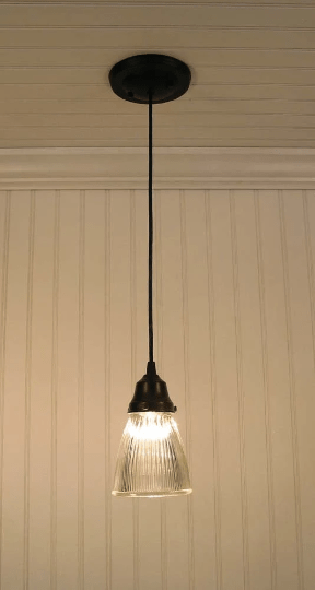 Glass pendant light with ribbed shade, hanging against paneled wall.