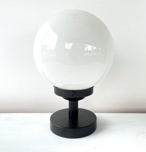 White globe table lamp with matte black base, shown on a white surface.
