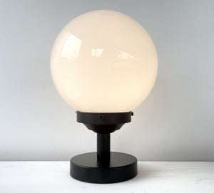 White milk glass globe table lamp with a black metal base, shown on a white surface.