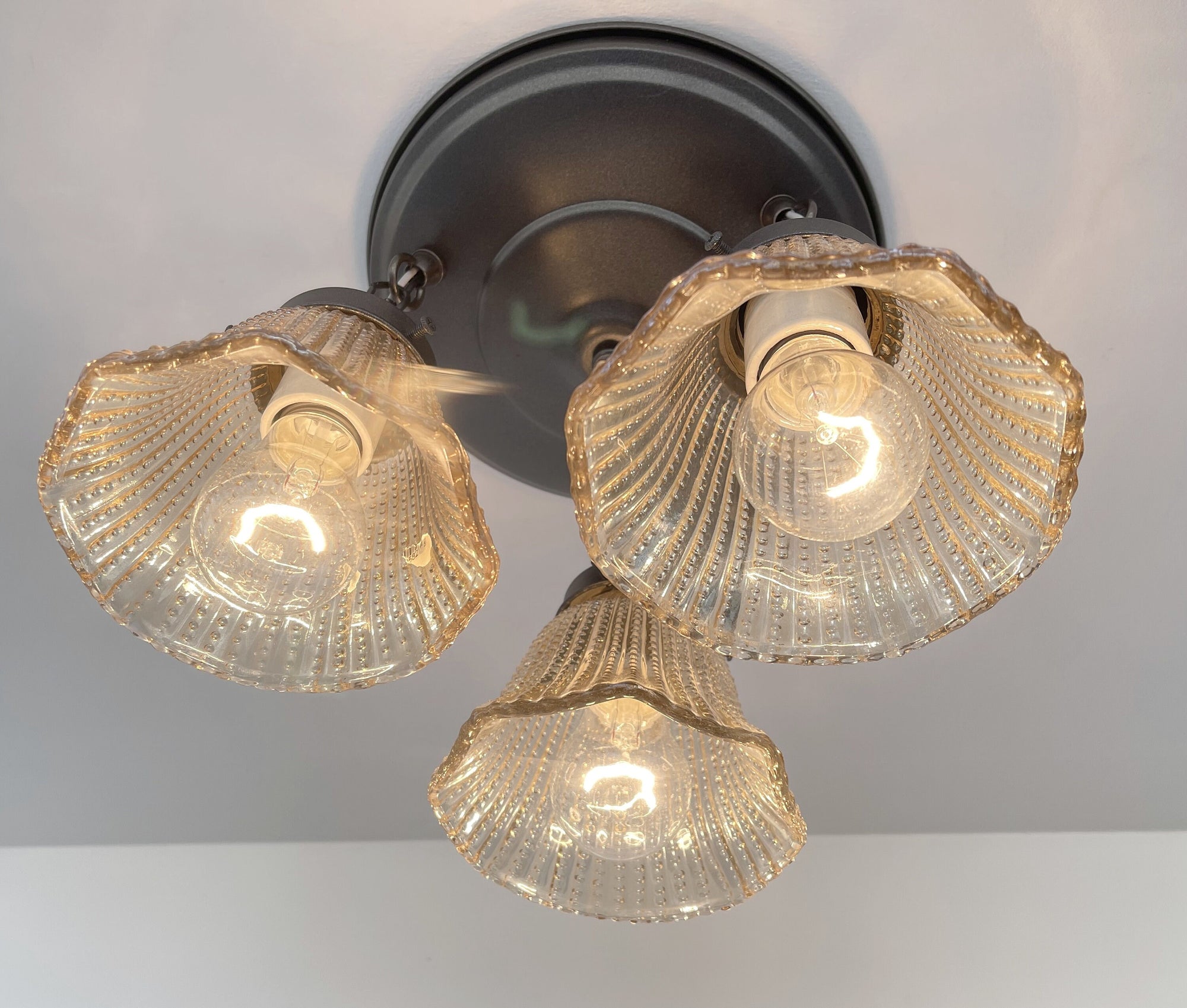 Amber glass ceiling light fixture with hobnail detailing, illuminated.
