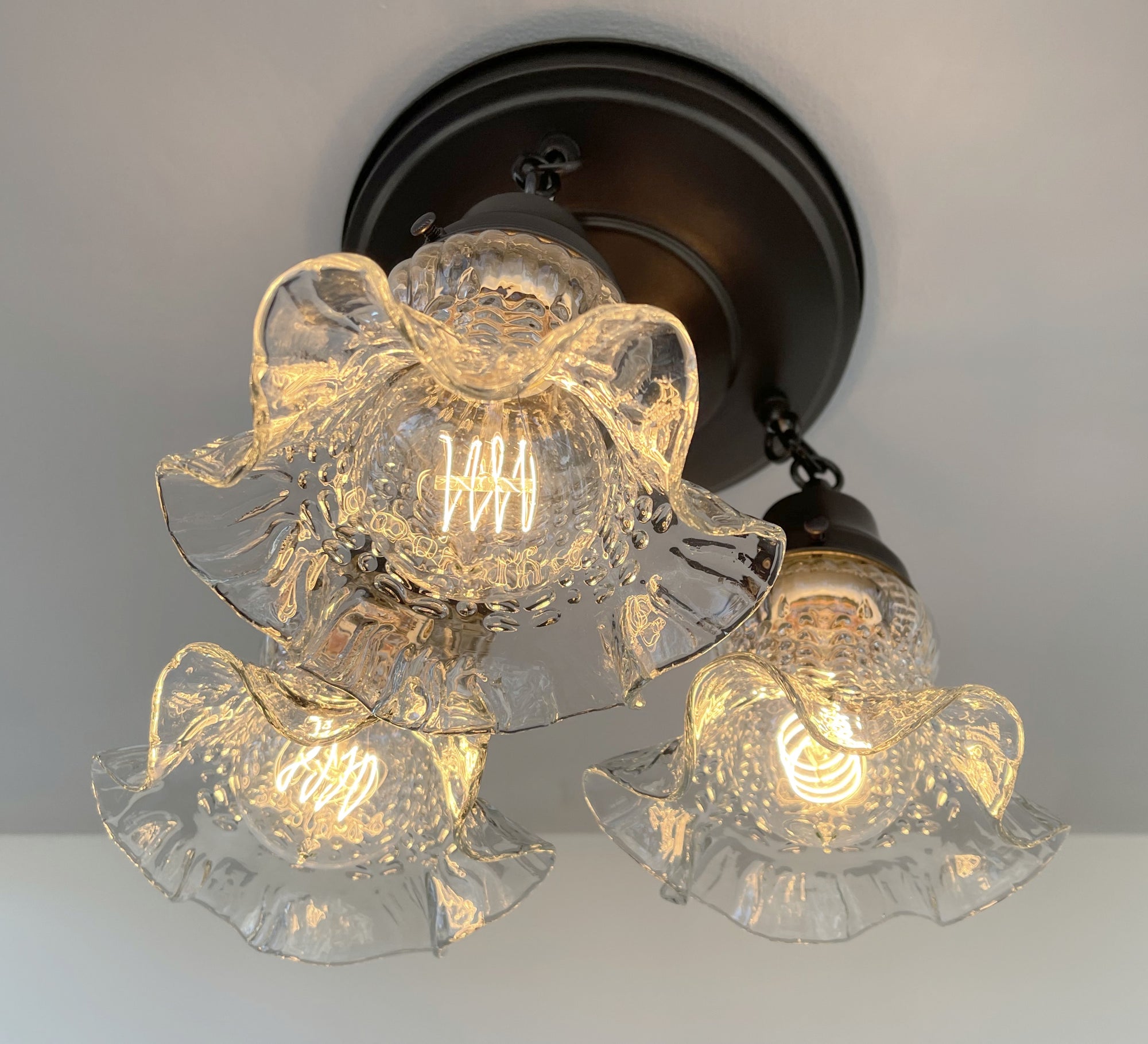 Three-light hobnail glass ceiling fixture with ruffled shades, illuminated, installed on a neutral ceiling.
