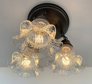 Three-light hobnail glass ceiling fixture with ruffled shades, illuminated, installed on a neutral ceiling.
