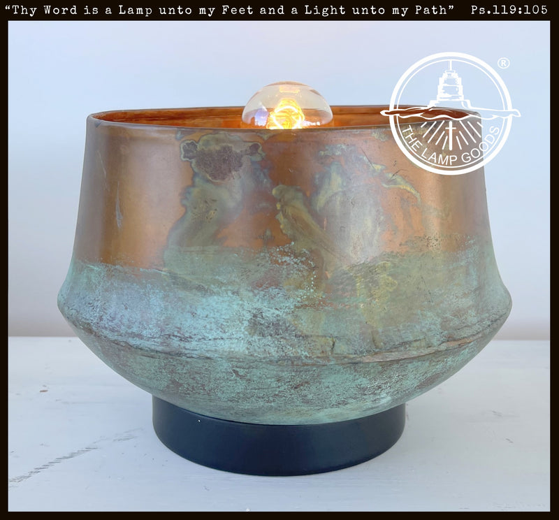 Handcrafted copper table lamp with a rustic patina, featuring a vintage-style bulb.
