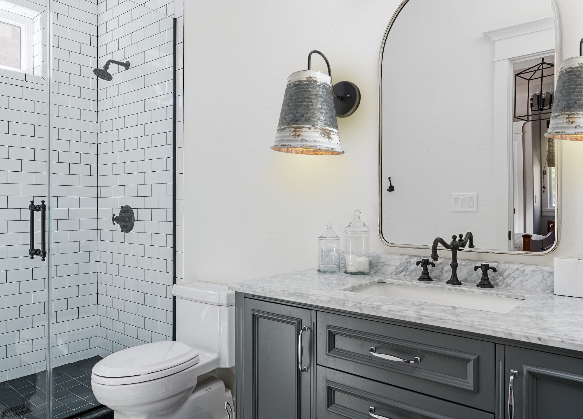 Distressed metal farmhouse wall sconce, illuminating a gray vanity in a modern bathroom.
