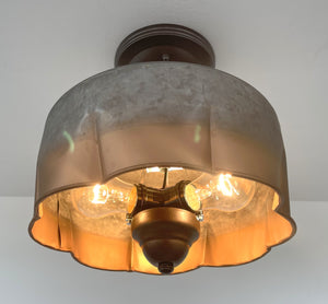 Three-light ceiling fixture, galvanized metal shade with copper accents, illuminating a room.
