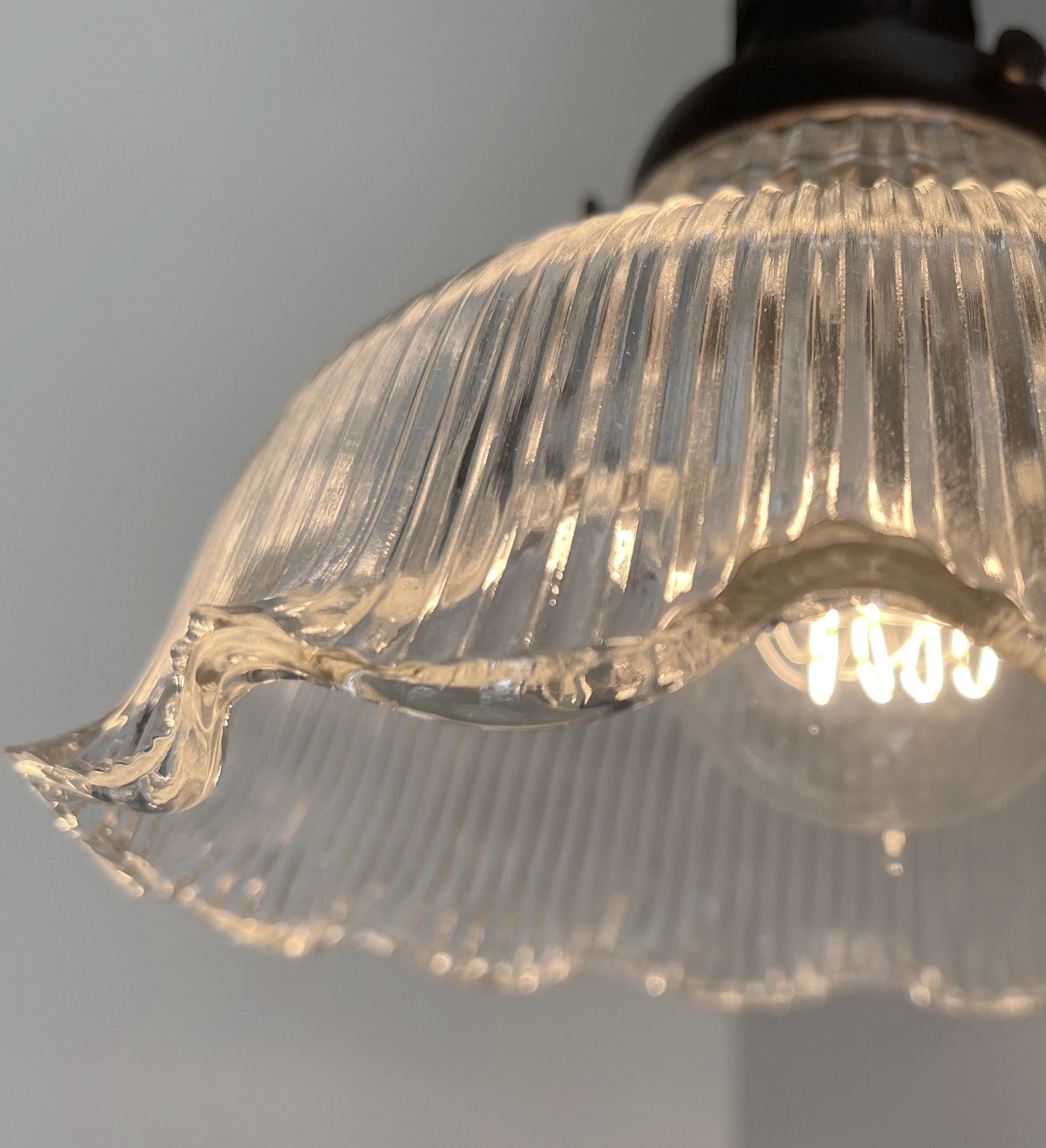 Close-up of an illuminated vintage glass wall sconce, showcasing its ribbed texture and scalloped edge.
