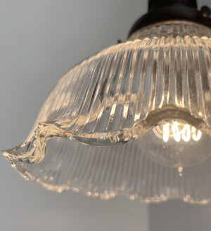 Close-up of an illuminated vintage glass wall sconce, showcasing its ribbed texture and scalloped edge.
