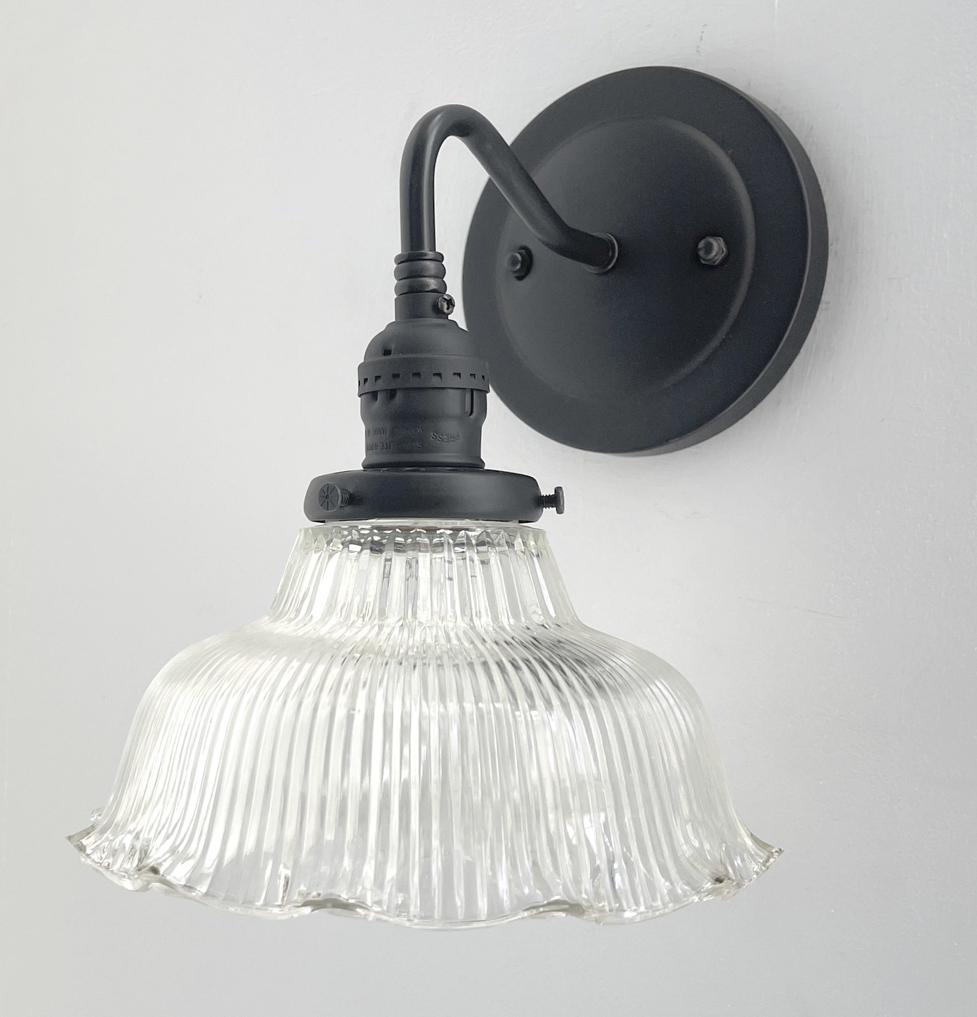 Clear glass ribbed wall sconce with a matte black metal base, mounted on a white wall.
