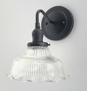 Clear glass ribbed wall sconce with a matte black metal base, mounted on a white wall.
