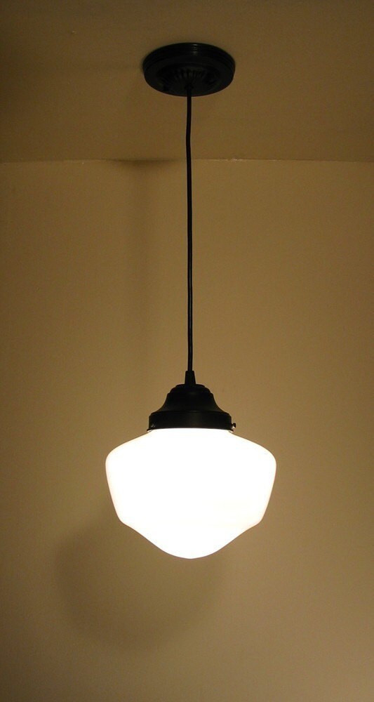 White milk glass pendant light fixture with black metal accents, illuminated against a beige wall.
