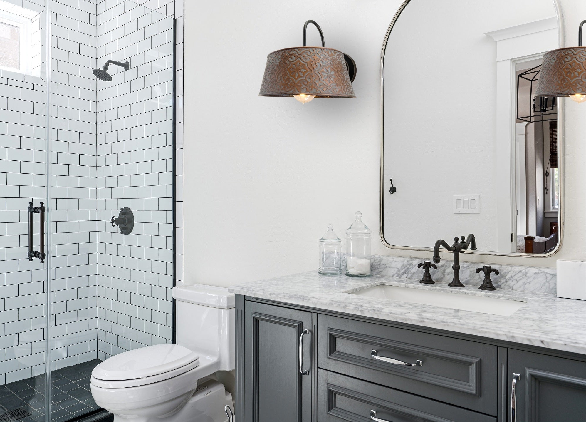 Copper wall sconce with ornate pattern, illuminating a modern bathroom vanity.
