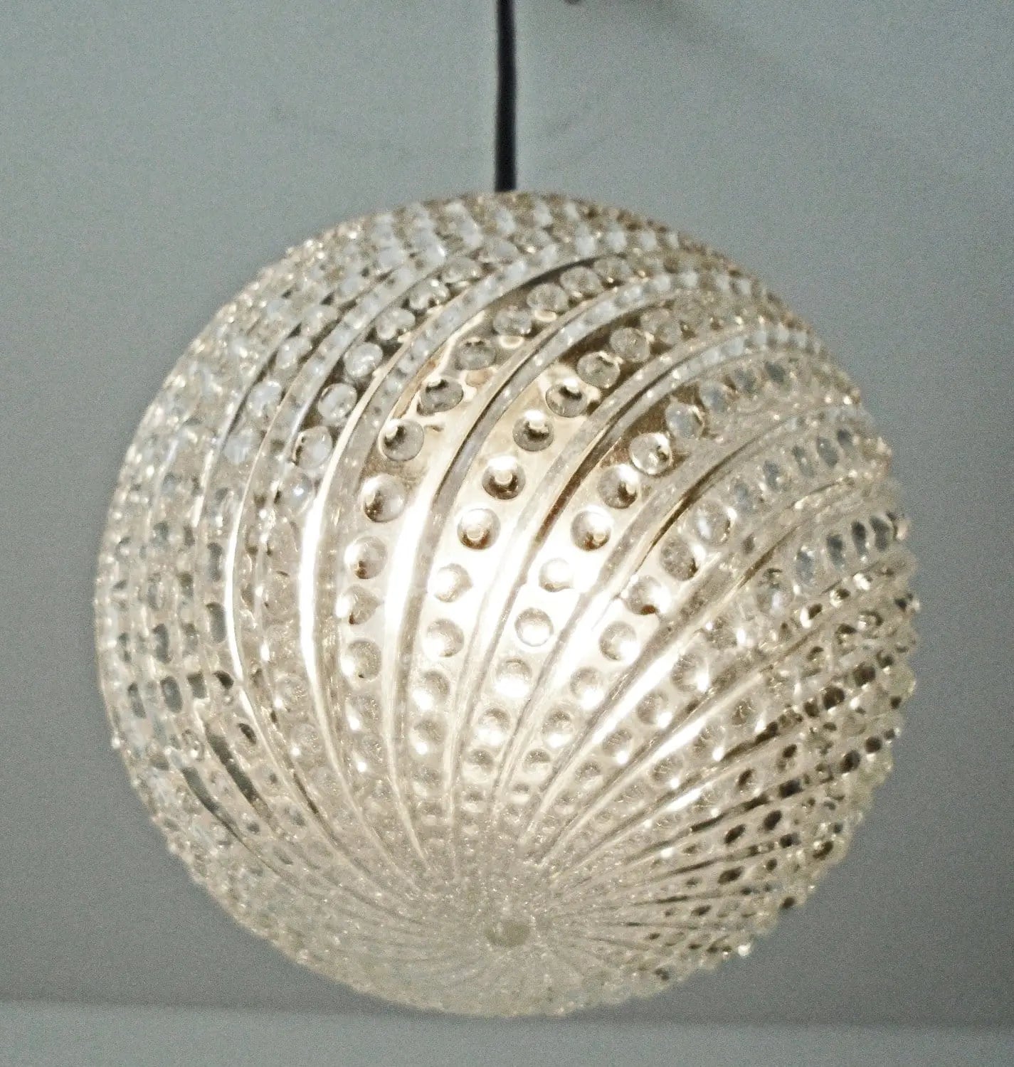 Clear glass pendant light fixture with hobnail swirl design, hanging against a neutral background.
