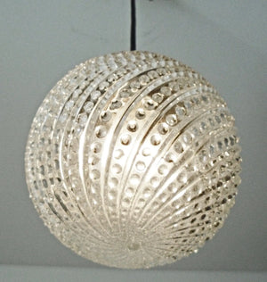 Clear glass pendant light fixture with hobnail swirl design, hanging against a neutral background.
