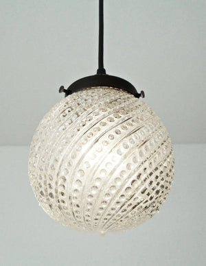 Clear glass pendant light with hobnail swirl pattern, black metal fixture.
