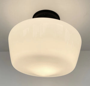Milk glass ceiling light fixture with dark bronze mounting plate, softly illuminating a room.
