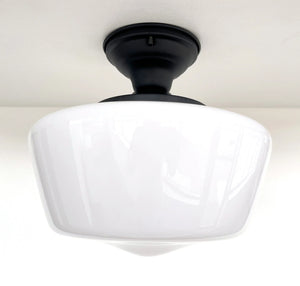 White milk glass ceiling light fixture with a black metal base, installed on a white ceiling.
