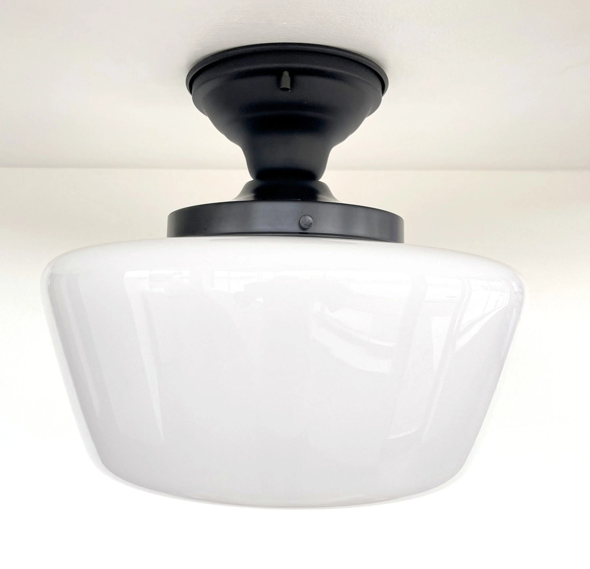 White milk glass ceiling light fixture with a black metal frame, shown installed on a white ceiling.
