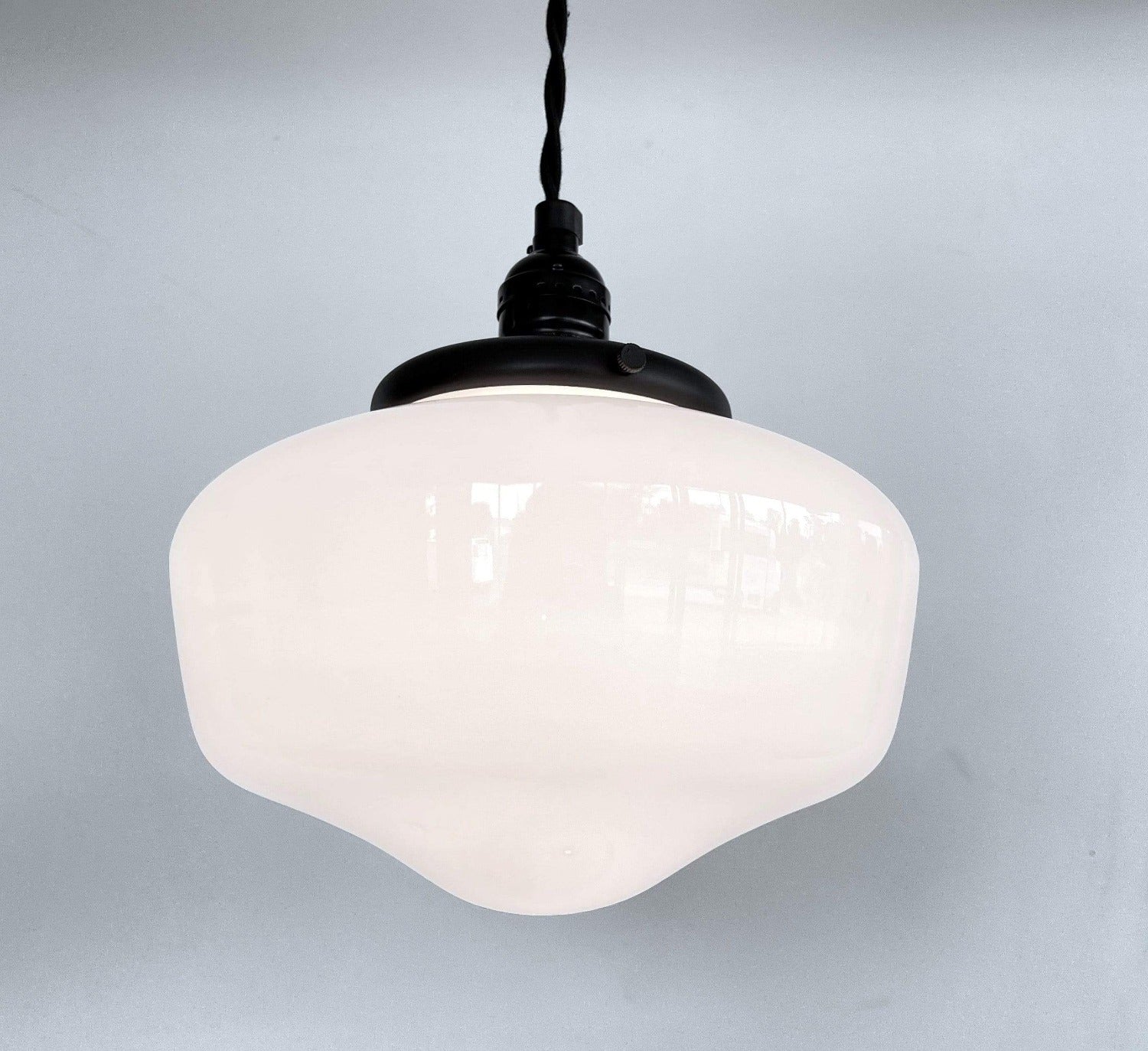 Milk glass pendant light fixture with black metal accents, hanging against a light gray wall.
