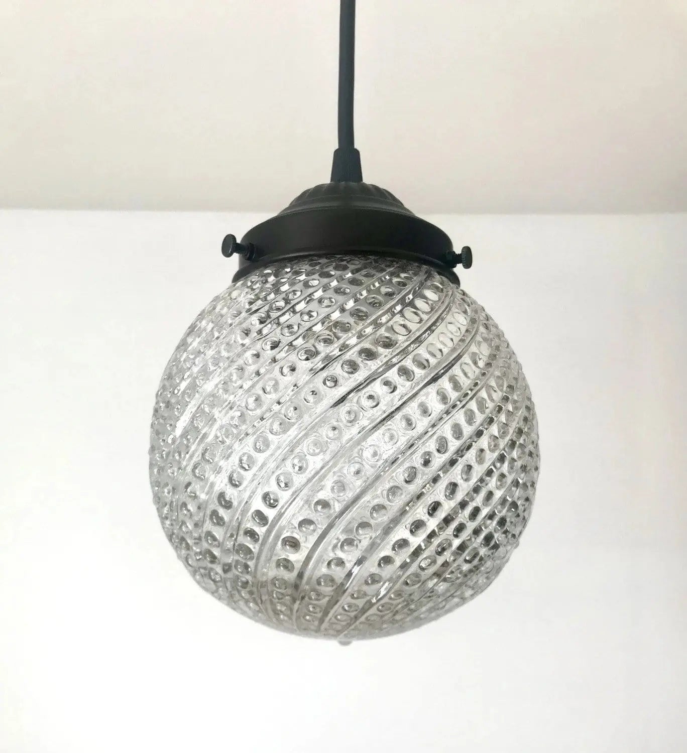Clear glass pendant light with hobnail swirl pattern and dark metal fixture.
