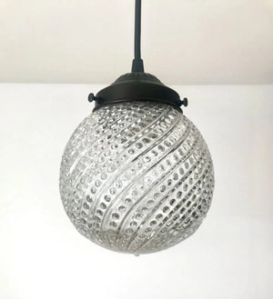 Clear glass pendant light with hobnail swirl pattern and dark metal fixture.
