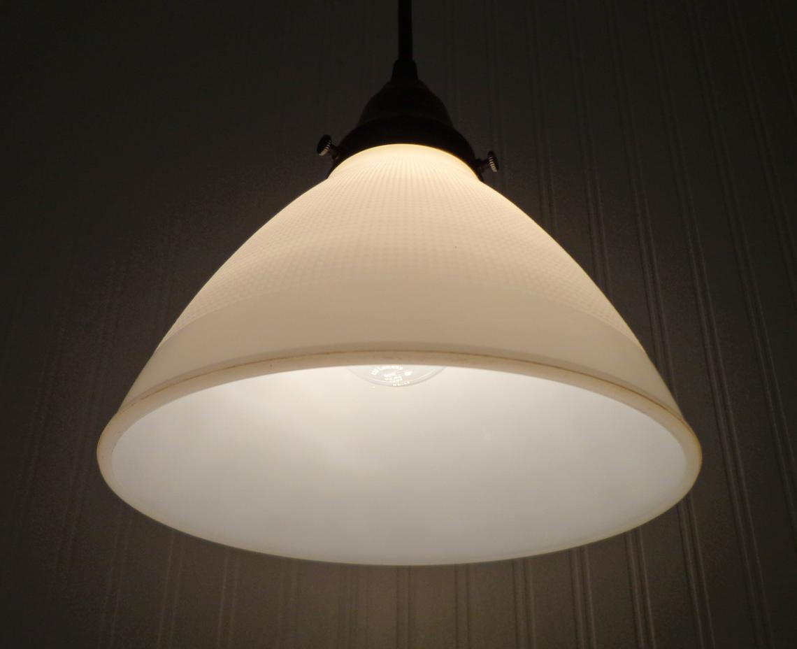 Softly lit milk glass pendant light fixture hanging against a dark wall.
