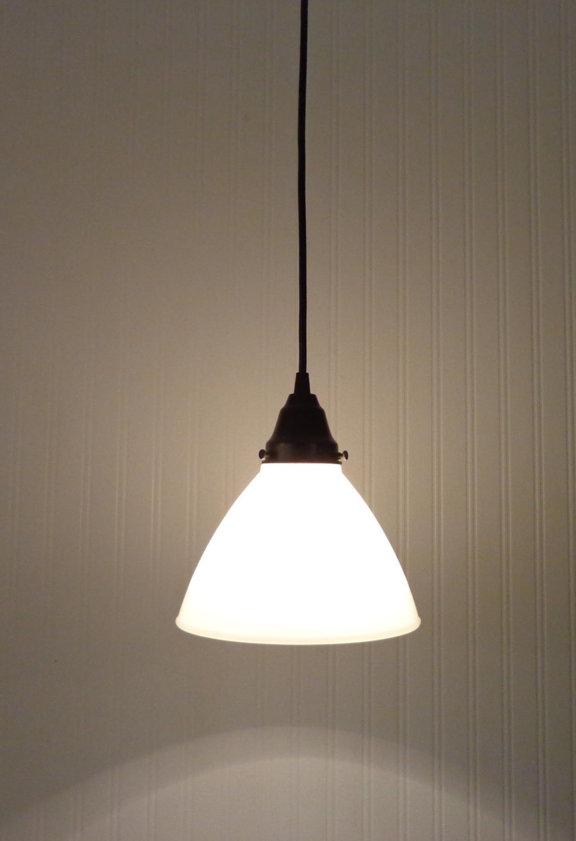 Illuminated milk glass pendant light fixture against a textured wall.

