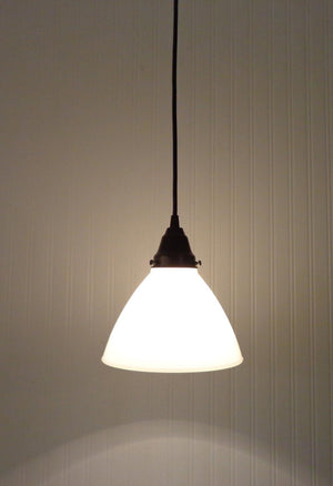 Illuminated milk glass pendant light fixture against a textured wall.
