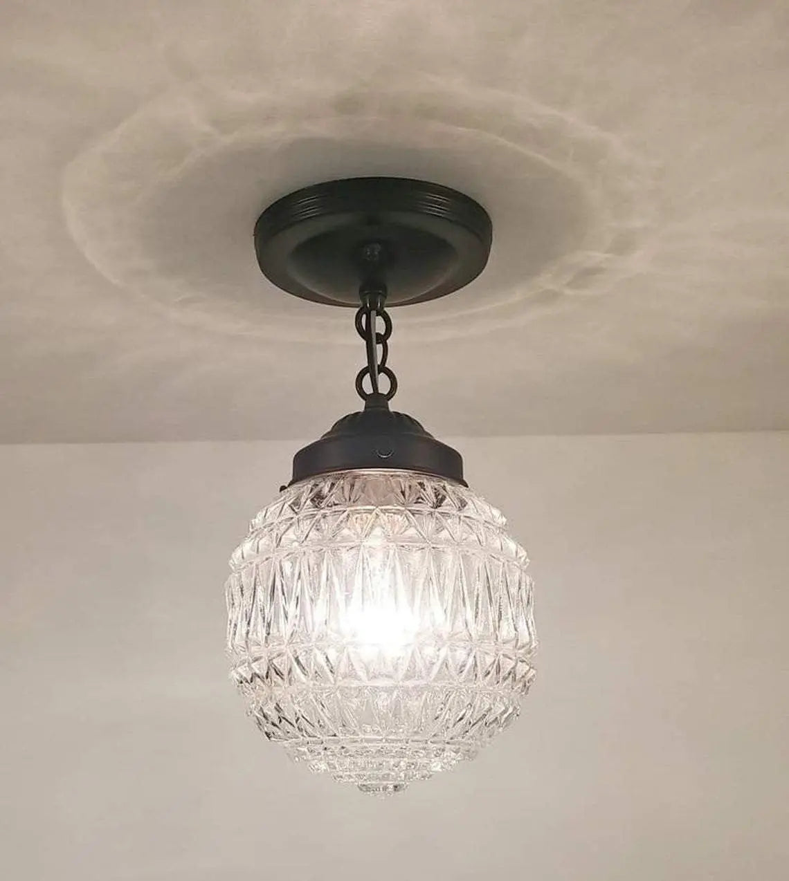 Clear glass globe pendant light fixture with a dark bronze finish, hanging from a ceiling.
