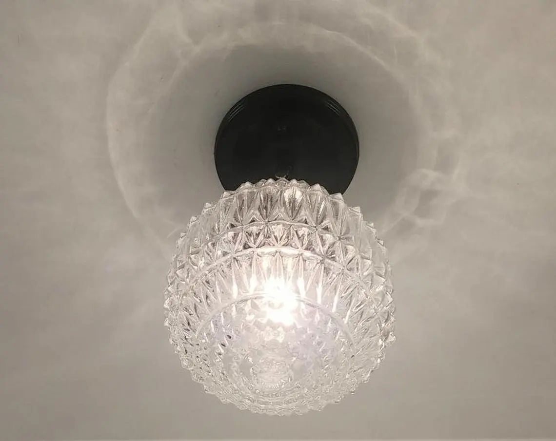 Clear glass ceiling light fixture with a faceted globe shade and black base.
