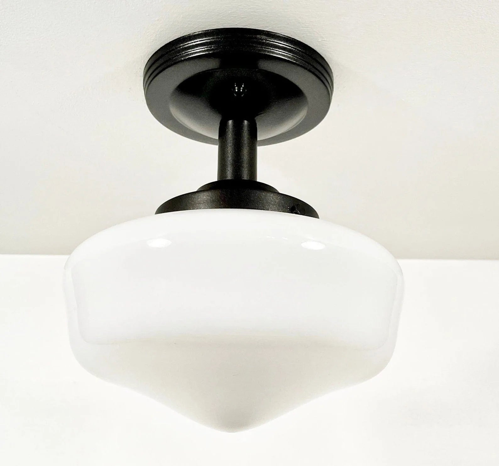 White milk glass ceiling fixture with a black metal base, installed on a white ceiling.
