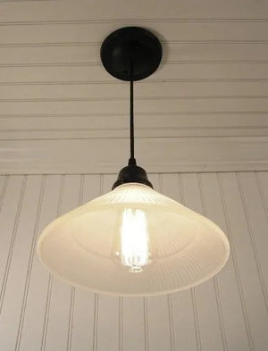 Frosted glass pendant light fixture with ribbed detailing, illuminated by Edison bulb, hanging from black cord against white paneled walls.
