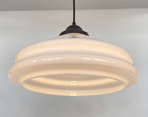 Cream-colored milk glass pendant light fixture with layered design, illuminating a neutral background.
