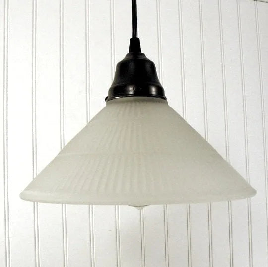 Frosted glass pendant light with ribbed texture, hanging against white paneled wall.
